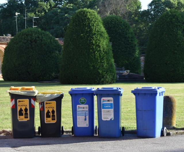 Una fila di bidoni per la raccolta differenziata di plastica e carta sul bordo di un prato, in una foto di repertorio