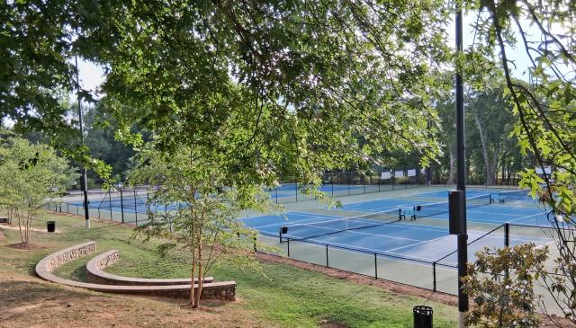Campi da tennis in cemento blu all’aperto fra gli alberi: foto di repertorio, non è il Magna Grecia Tennis Center